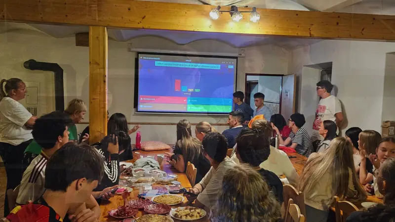 Todo el grupo sentado a la mesa siguiendo un Kahoot proyectado durante la noche intercultural