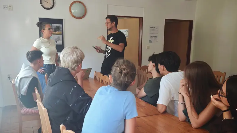 Un facilitador de pie hablando al grupo sentado alrededor de una mesa